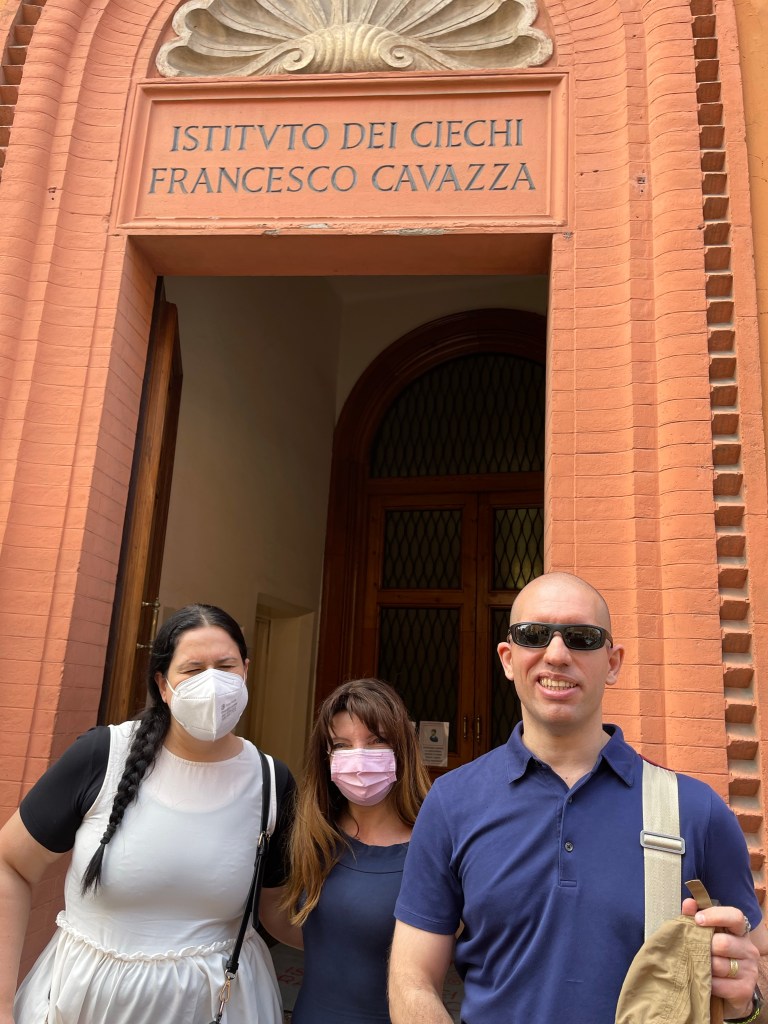 Roberto assieme alla tiflologa Debora Tramentozzi e alla Dottoressa Loretta Secchi, posano felici all’ingresso dell’Istituto Cavazza