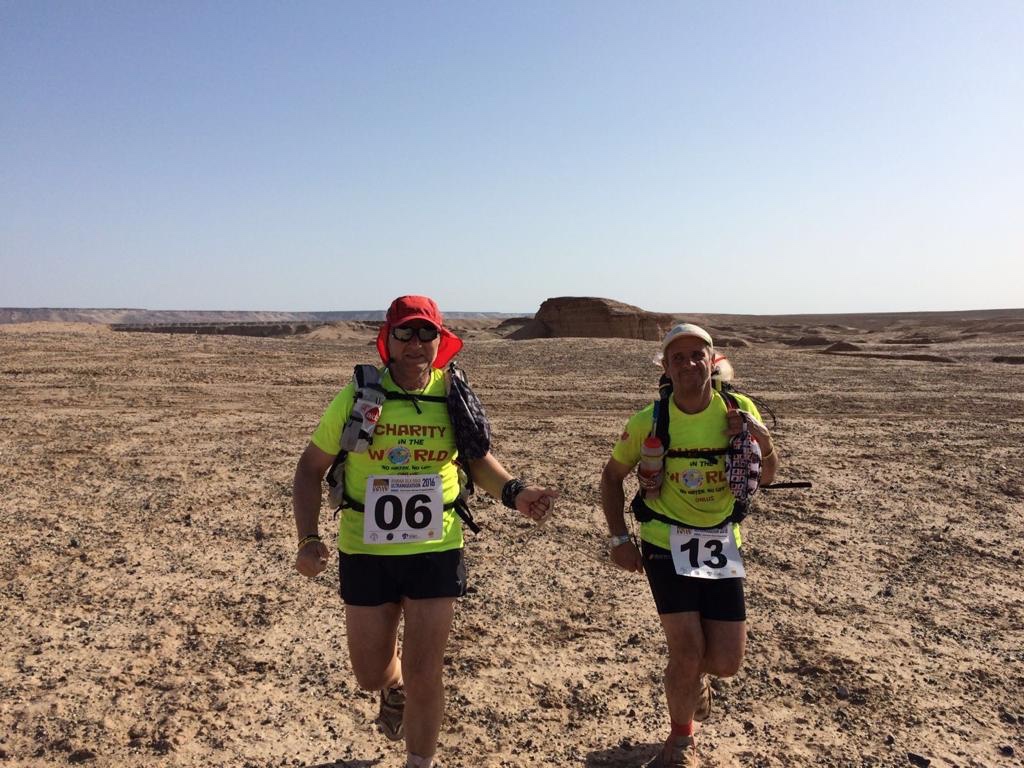 Tullio e Raffaele corrono nel deserto iraniano.magliette e pantaloncini corti con i numeri 6 e 13. Alle spalle due zaini.