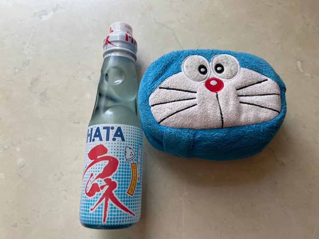 Bottiglia di Lamune con il collo a merluzzo per non fr cadere la sfera. Accanto un porta oggetti a forma di Doraemon