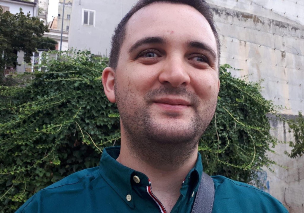 Michele posa sorridente in unparco, indossa una camicia verde 